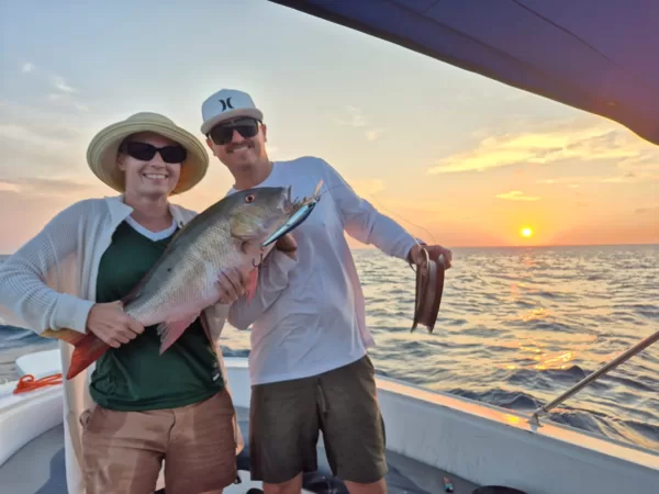 Casal segurando um peixe ao pôr do sol em um charter de pesca em Aruba